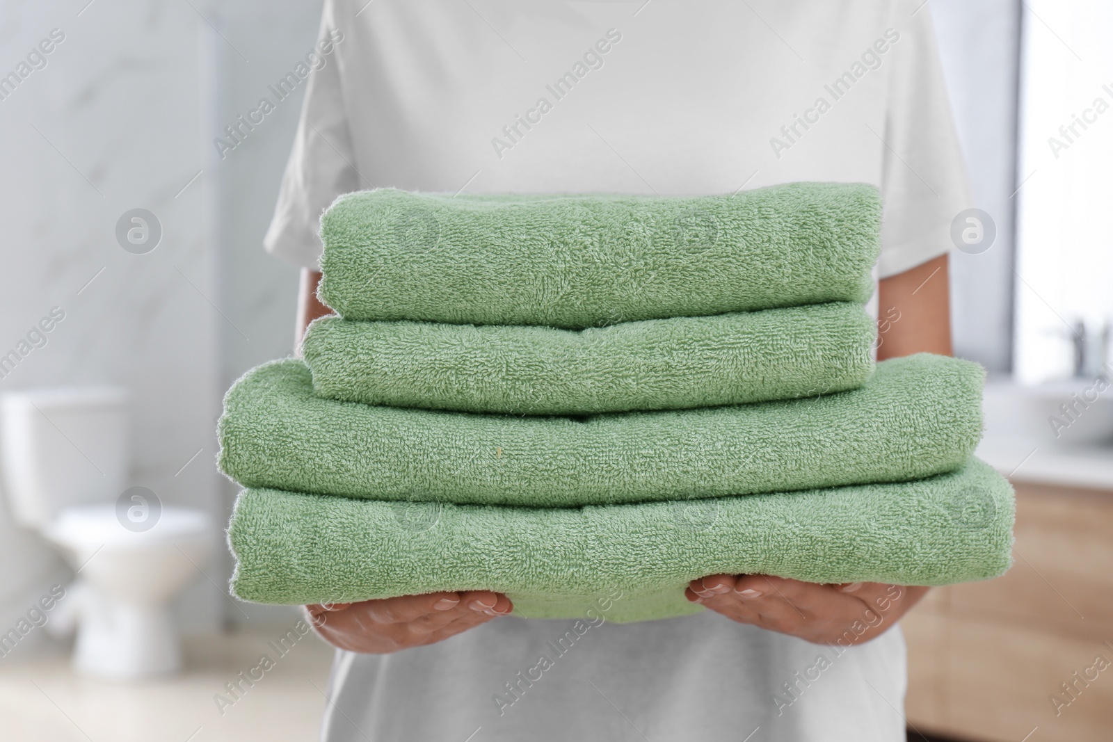 Photo of Woman holding fresh towels in bathroom, closeup