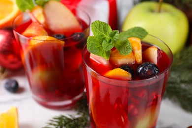 Photo of Aromatic Sangria drink in glasses, ingredients and Christmas decor on white marble table, closeup
