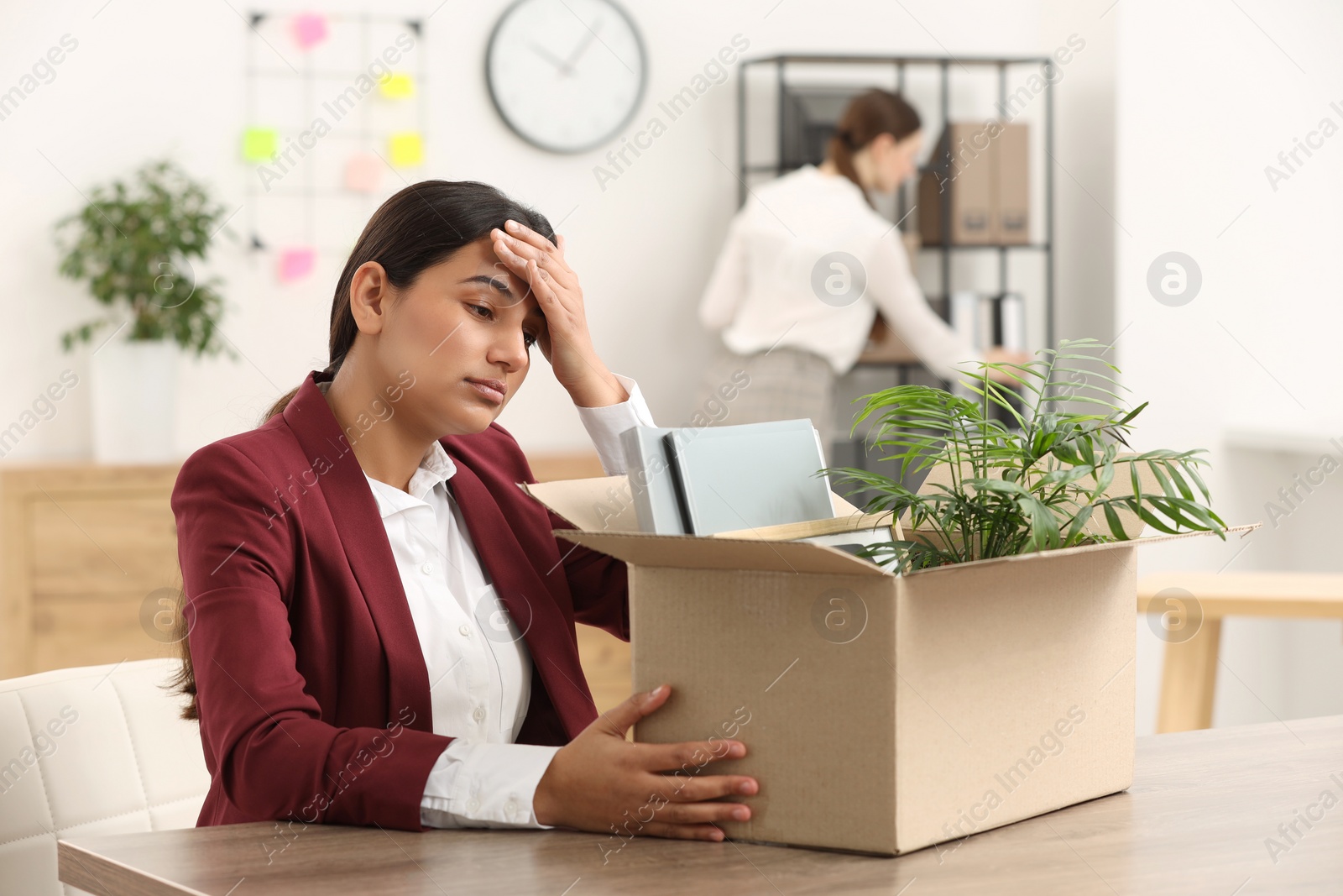 Photo of Unemployment problem. Frustrated woman with box of personal belongings at table in office