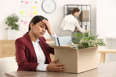 Photo of Unemployment problem. Frustrated woman with box of personal belongings at table in office