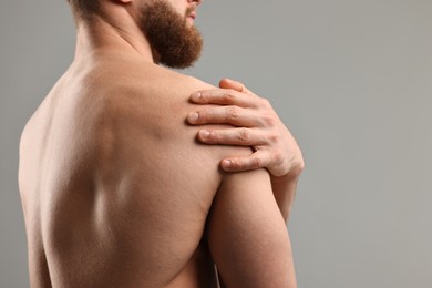 Man touching his shoulder on light grey background, closeup