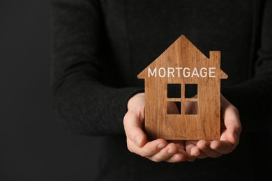 Image of Mortgage concept. Woman holding wooden house on dark background, closeup 