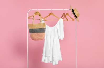 Photo of Rack with accessories and stylish white dress on wooden hangers against pink background