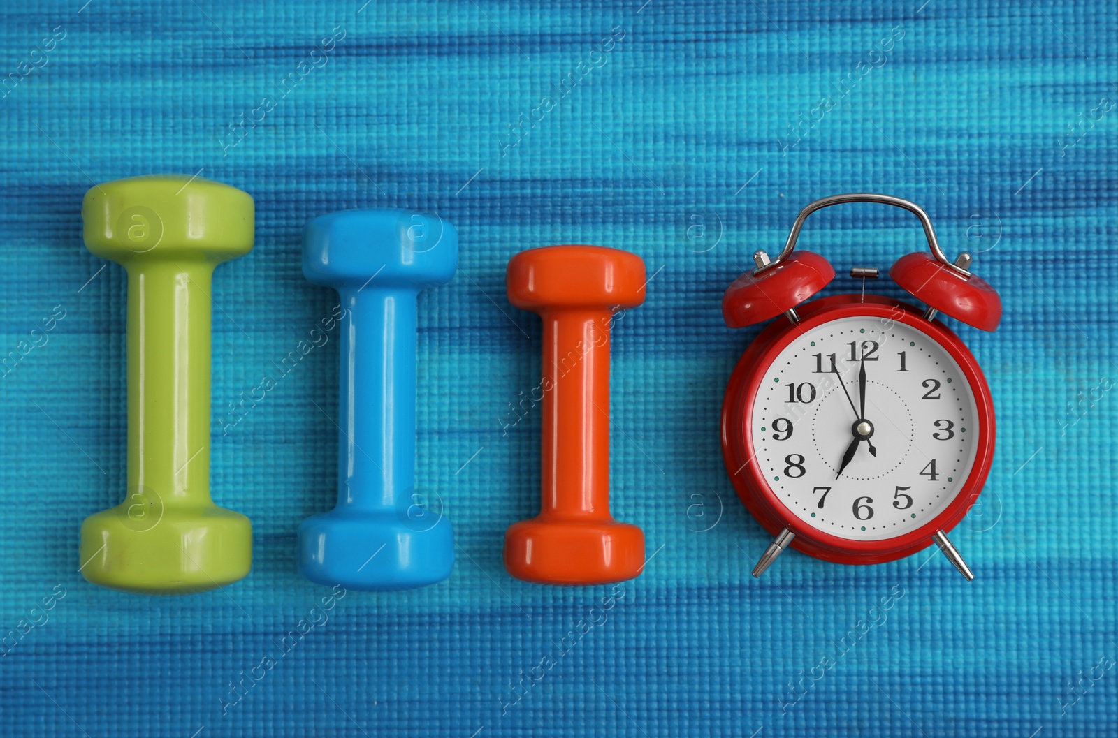 Photo of Alarm clock and dumbbells on blue yoga mat, flat lay. Morning exercise