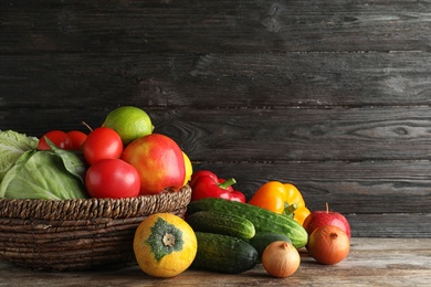 Basket with fresh fruits and vegetables on wooden table, space for text