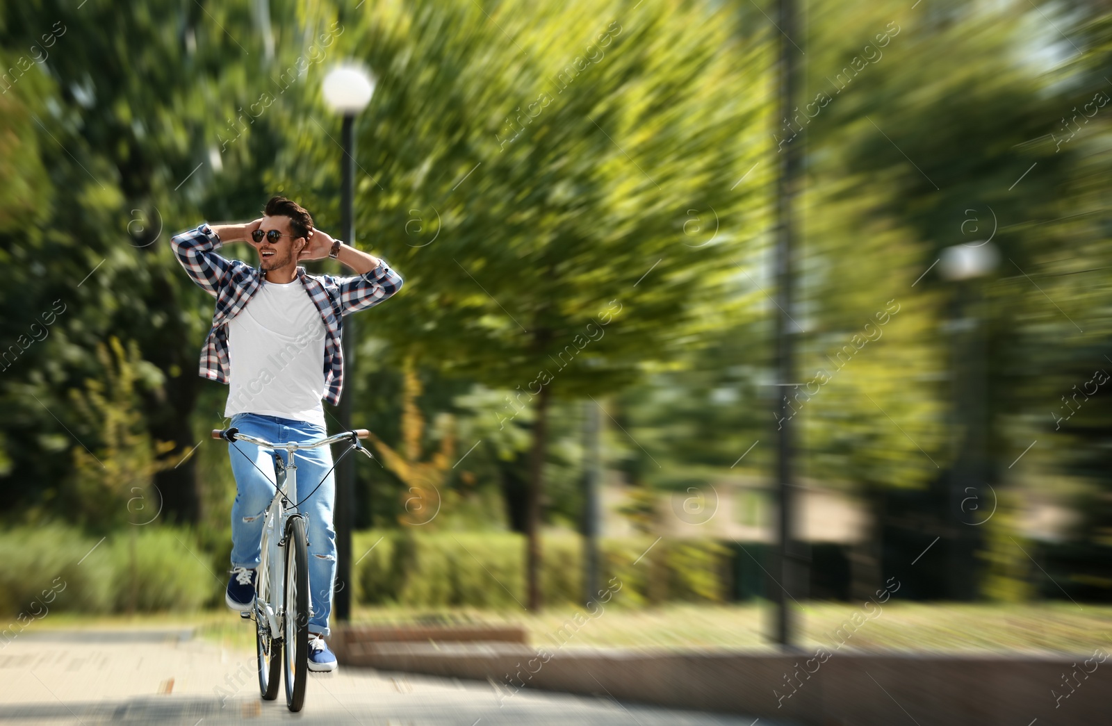 Image of Handsome young man riding bicycle in park, motion blur effect