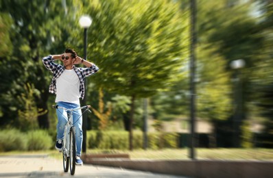 Image of Handsome young man riding bicycle in park, motion blur effect