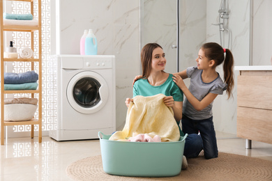 Mother and little daughter with clean laundry in bathroom