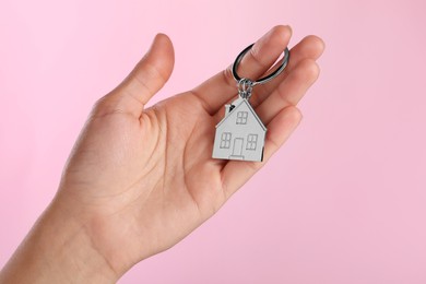Photo of Woman holding metallic keychain in shape of house on pink background, closeup