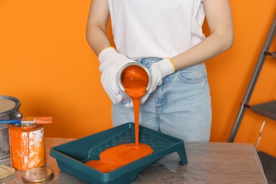 Woman pouring orange paint from can into tray at table, closeup