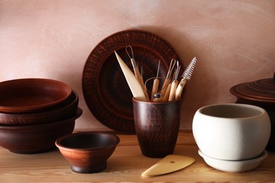 Set of different crafting tools and clay dishes on wooden table in workshop