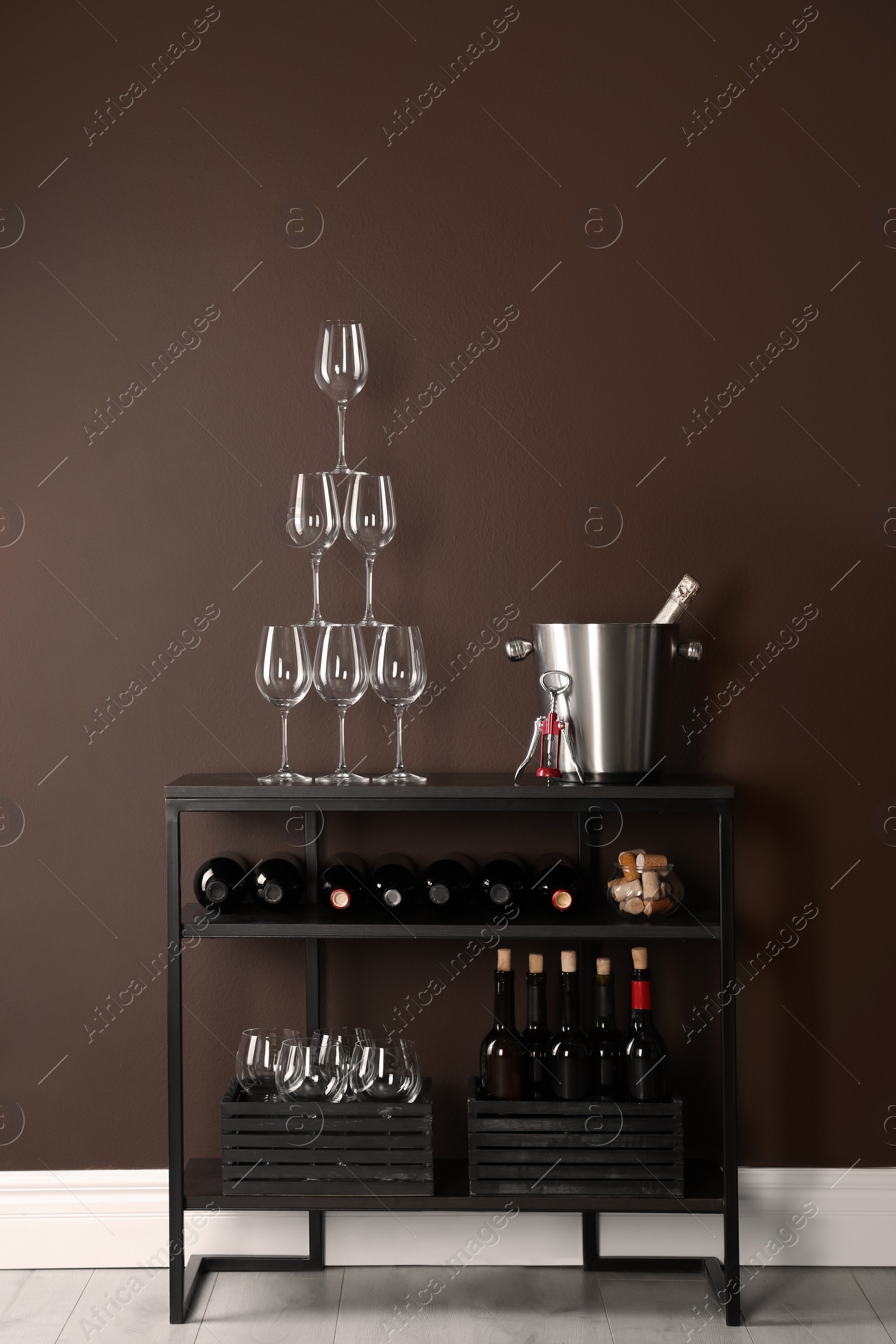 Photo of Rack with bottles of wine and glasses near brown wall