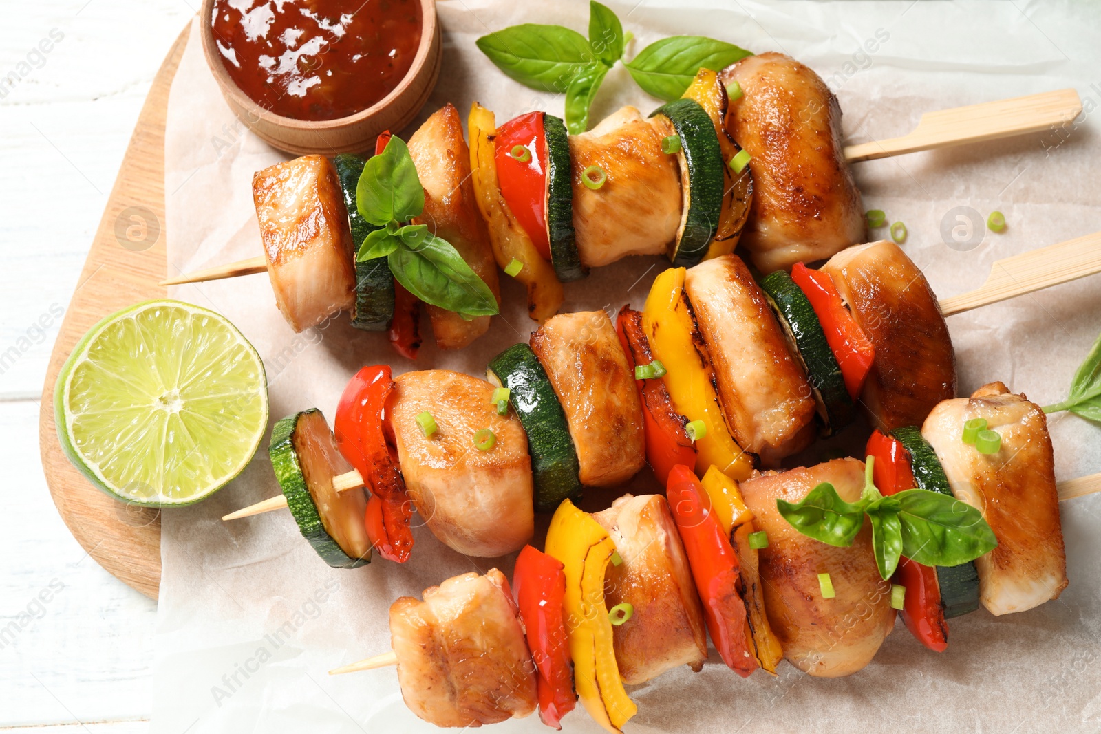 Photo of Delicious chicken shish kebabs with vegetables and lime on white wooden table, top view