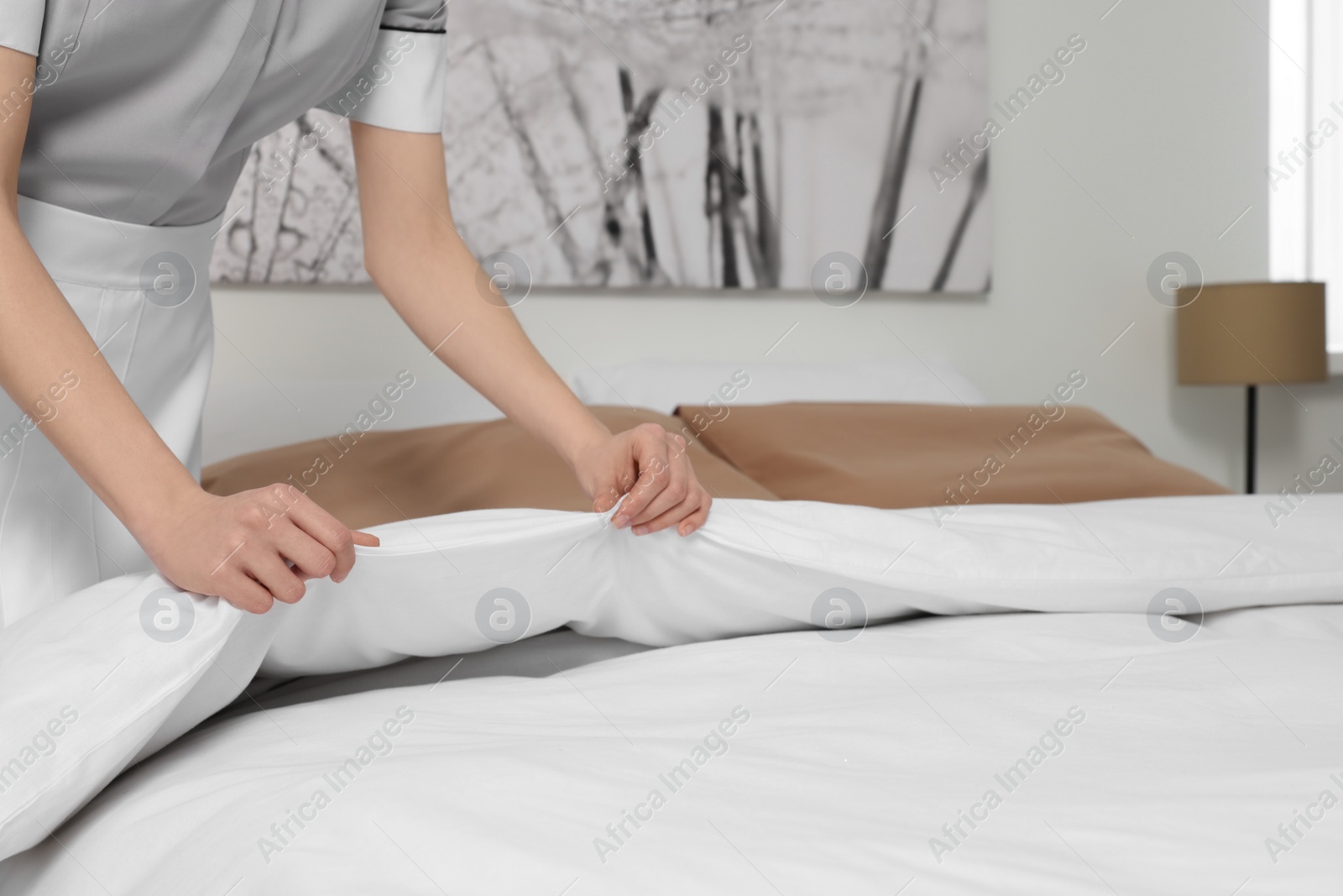 Photo of Young maid making bed in hotel room, closeup