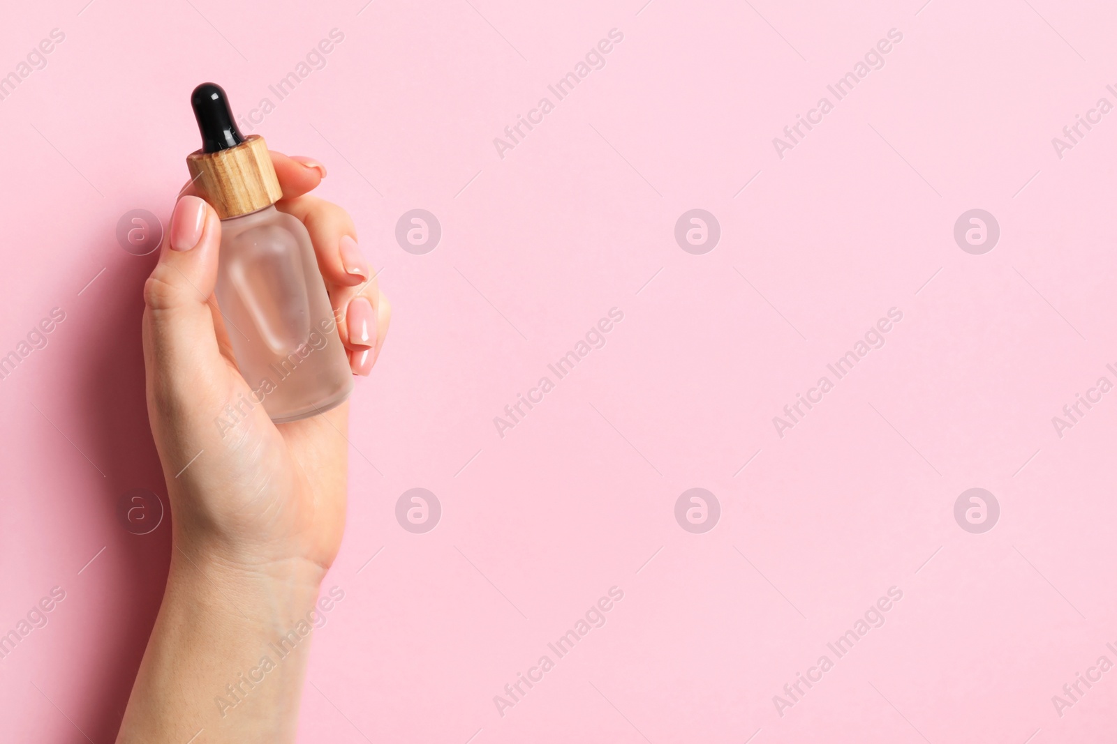 Photo of Woman holding bottle with serum on pink background, top view. Space for text