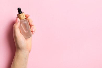 Photo of Woman holding bottle with serum on pink background, top view. Space for text