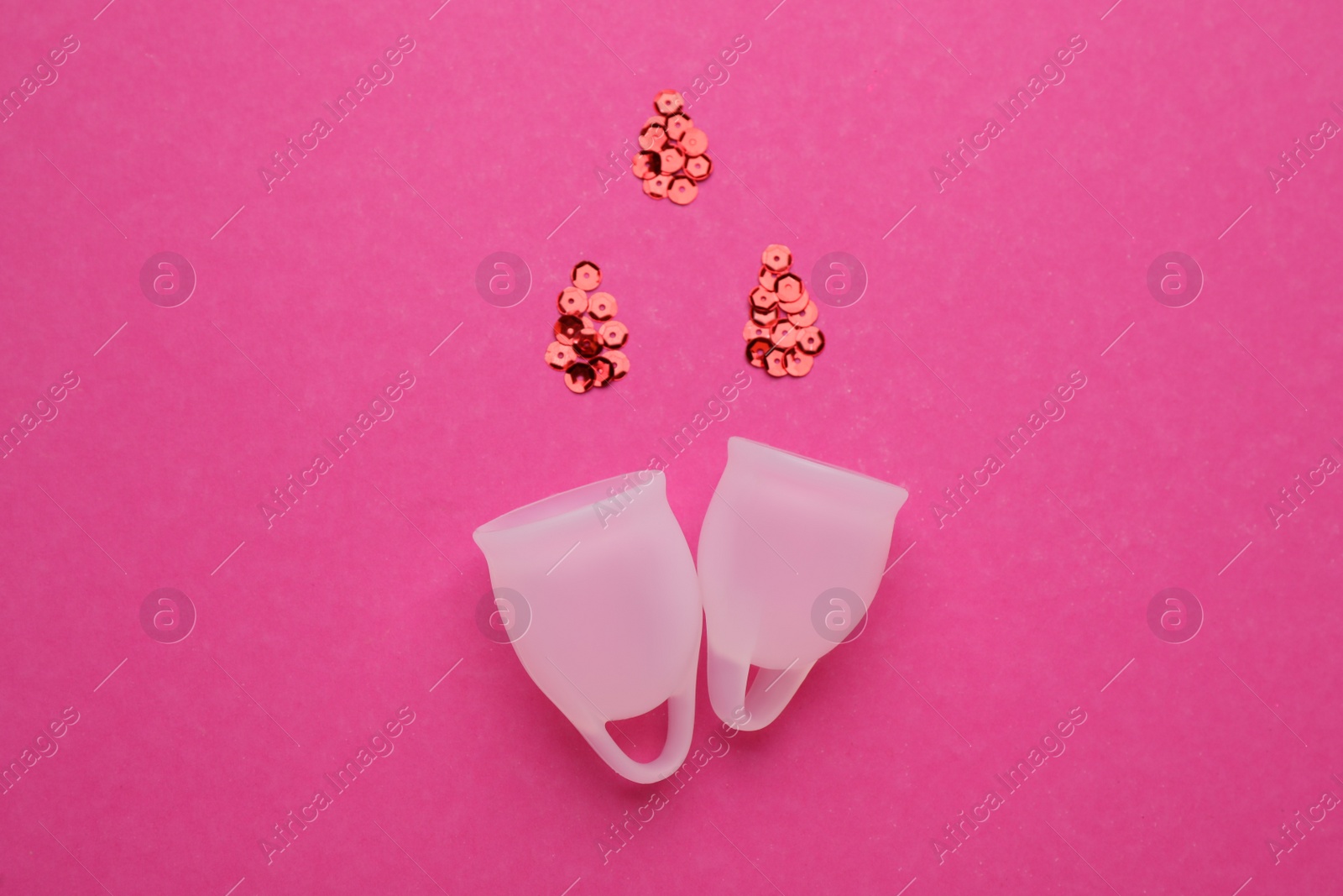 Photo of Menstrual cups near drops made of red sequins on pink background, flat lay