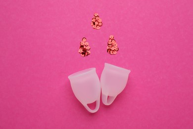 Photo of Menstrual cups near drops made of red sequins on pink background, flat lay
