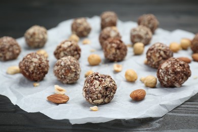 Delicious sweet chocolate candies and nuts on parchment paper, selective focus