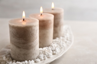 Photo of Plate with three burning candles and rocks on table, space for text