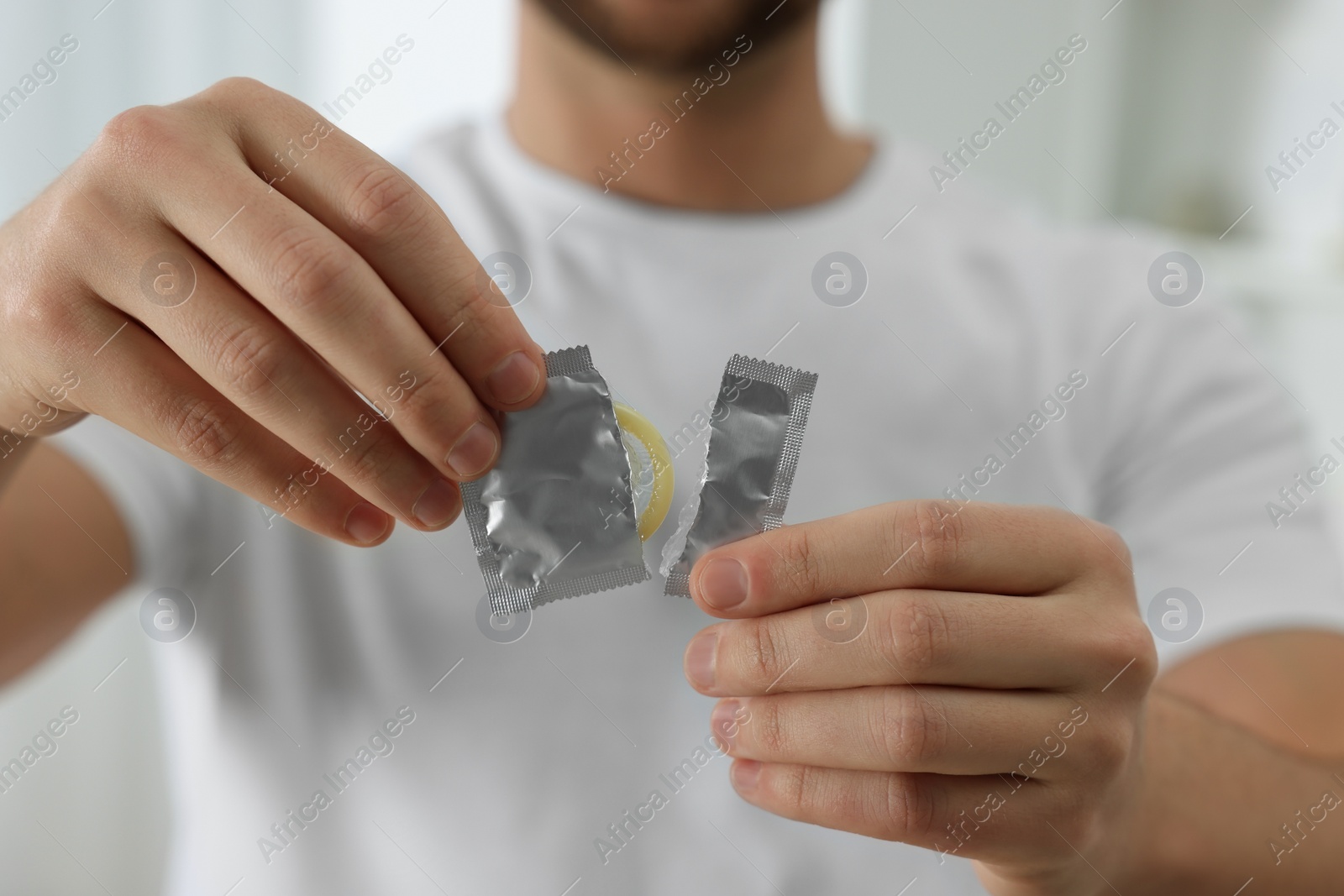 Photo of Closeup of man holding open pack with condom on blurred background