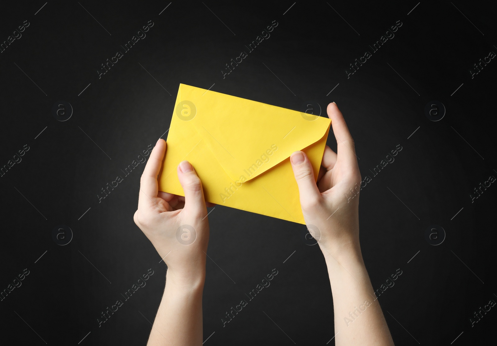 Photo of Woman holding yellow paper envelope on black background, closeup