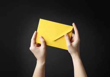 Photo of Woman holding yellow paper envelope on black background, closeup