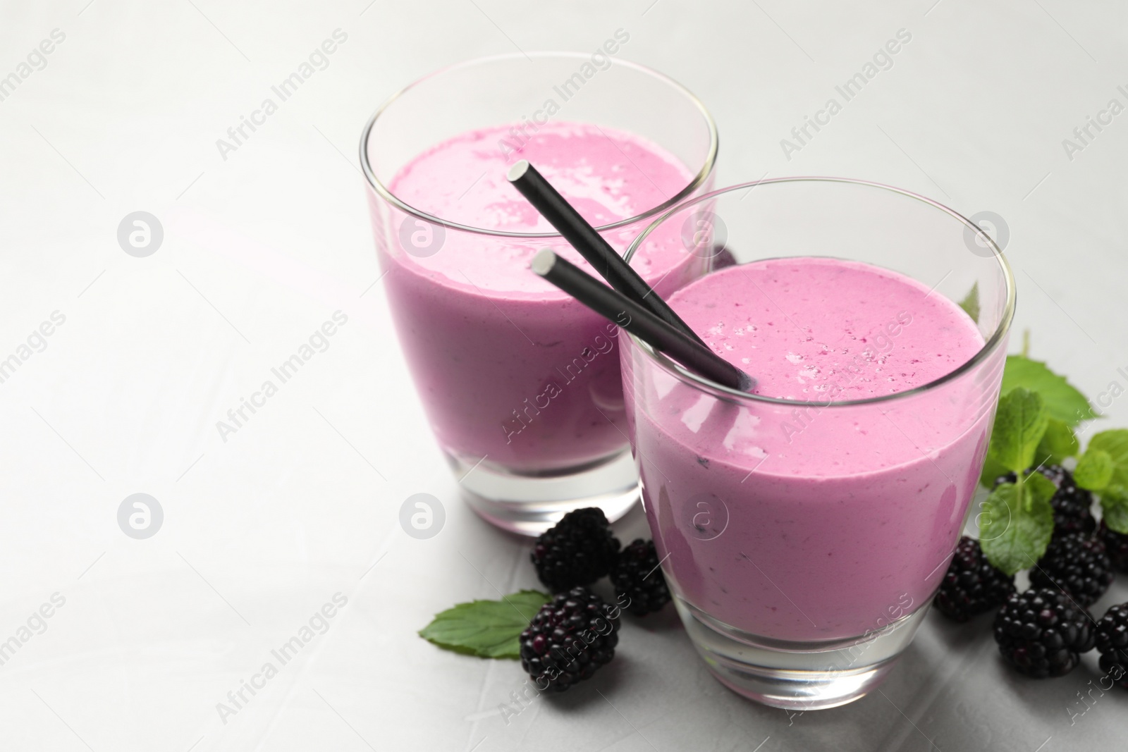 Photo of Delicious blackberry smoothie in glasses, fresh berries and mint on grey table