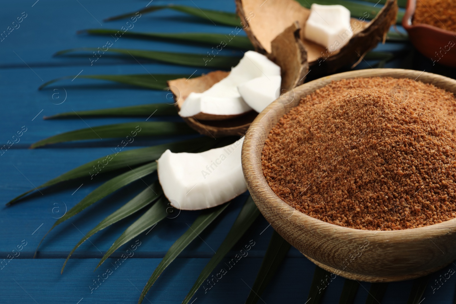 Photo of Natural coconut sugar in bowl on blue wooden table, space for text