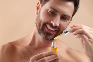 Smiling man with cosmetic serum on beige background, selective focus