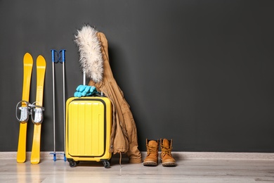 Suitcase, jacket and skis on floor against black wall, space for text. Winter vacation