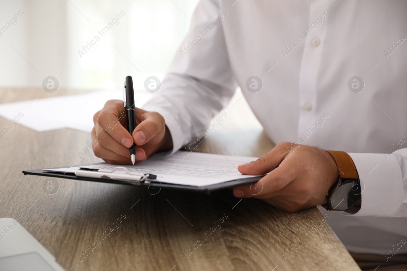 Photo of Businessman signing document at table indoors, closeup