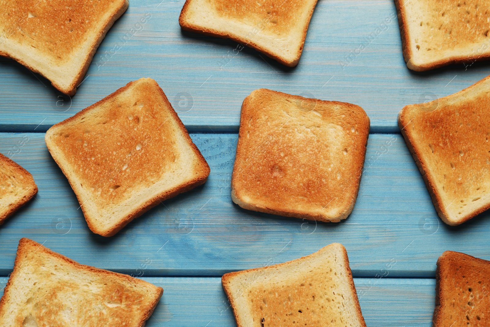 Photo of Slices of tasty toasted bread on turquoise wooden table, flat lay