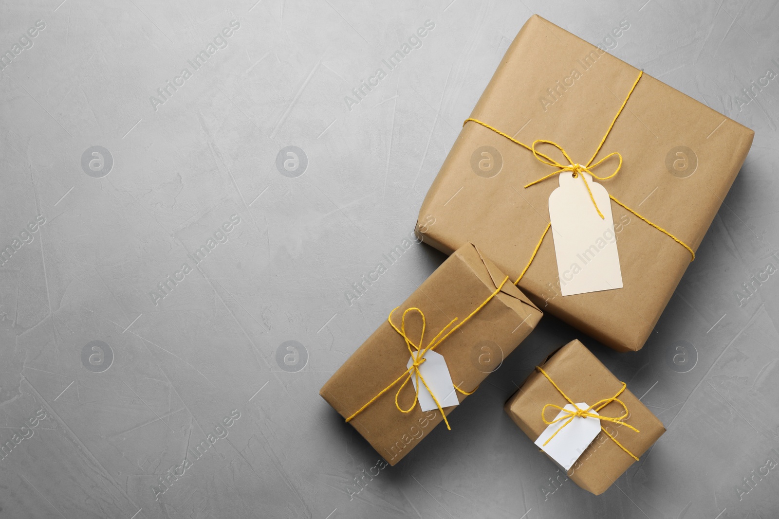 Photo of Parcels wrapped in kraft paper with tags on light grey table, flat lay. Space for text