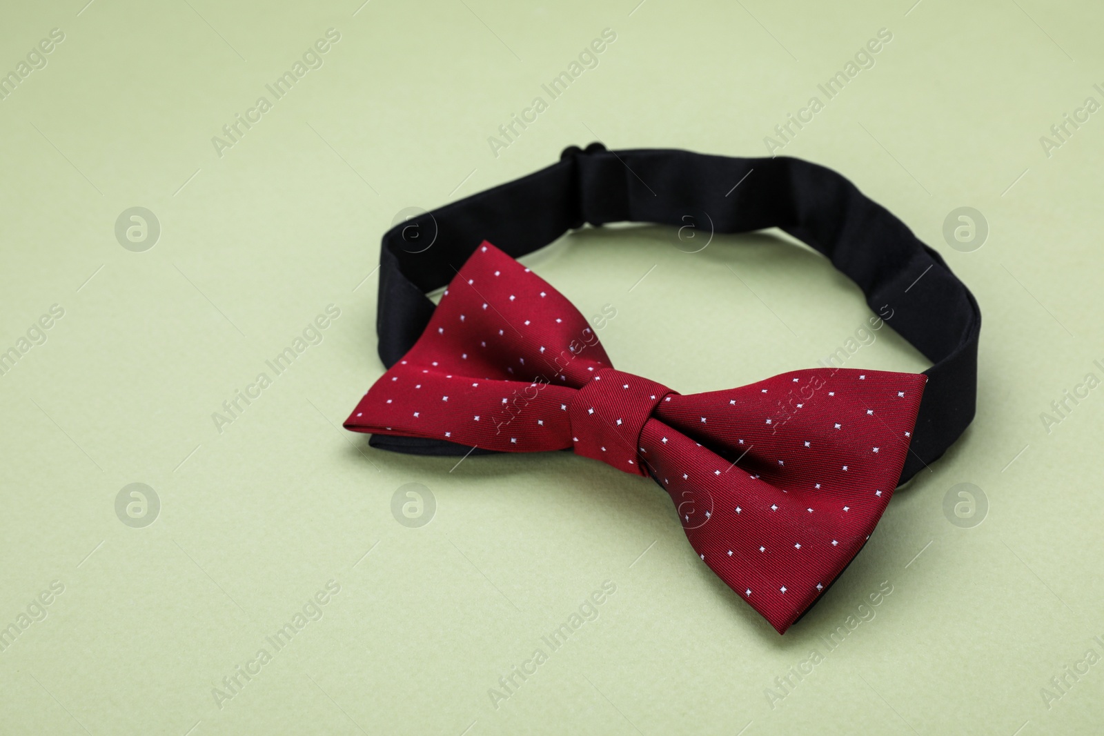 Photo of Stylish burgundy bow tie with polka dot pattern on pale green background, space for text