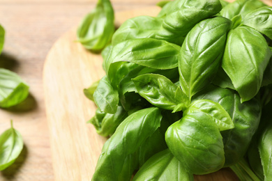 Photo of Fresh basil leaves on wooden board, closeup