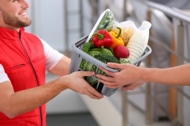 Photo of Courier giving plastic crate with products to customer at home, closeup. Food delivery service