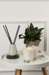 Burning soy candles, freshener and houseplant on white wooden table indoors