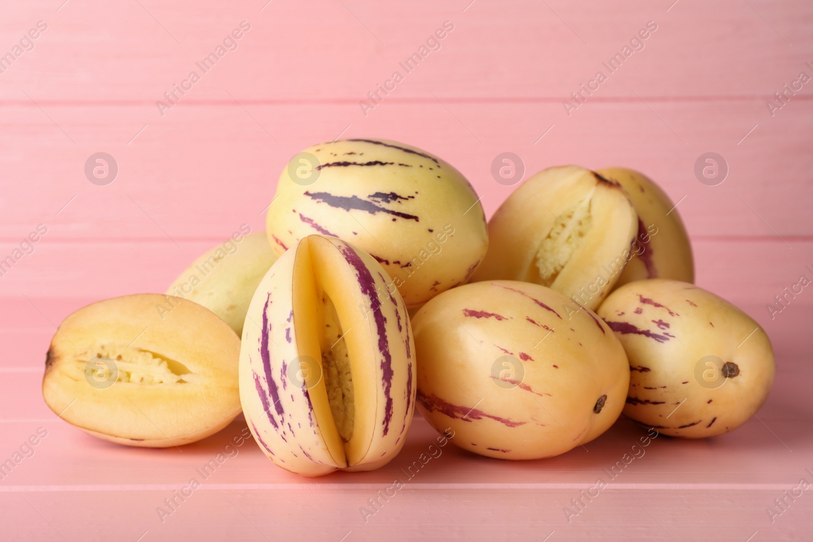 Photo of Whole and cut pepino melons on pink wooden table