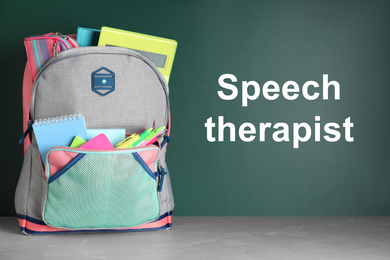 Stylish backpack with school stationery and text Speech Therapist on chalkboard 