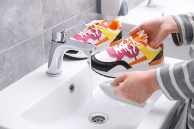 Photo of Woman washing stylish sneakers with brush in sink, closeup