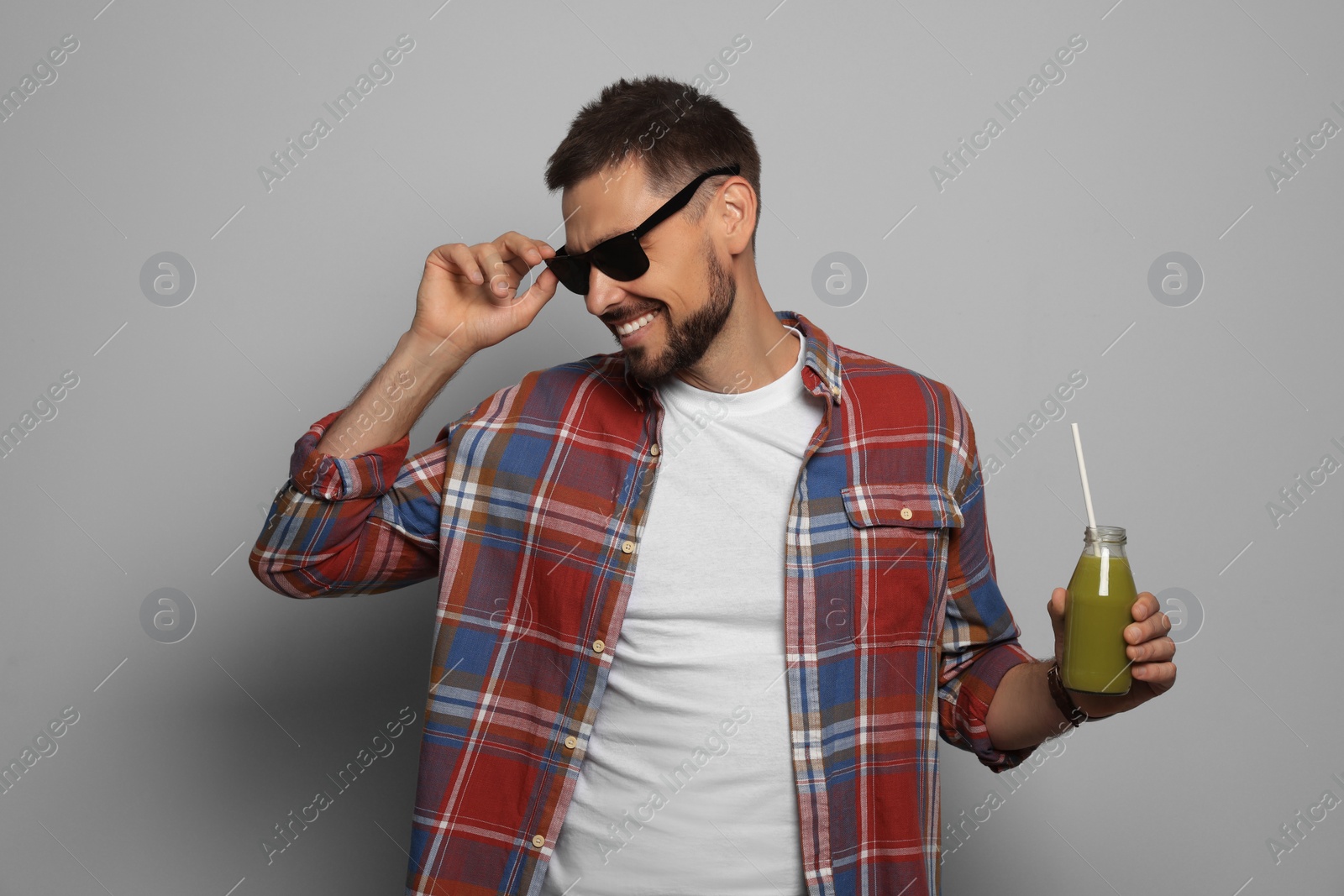 Photo of Happy man holding bottle of delicious juice on grey background