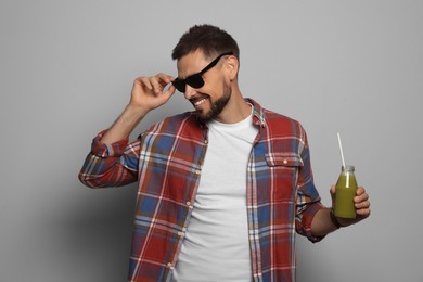 Happy man holding bottle of delicious juice on grey background