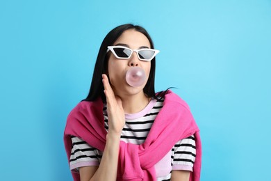 Photo of Fashionable young woman blowing bubblegum on light blue background