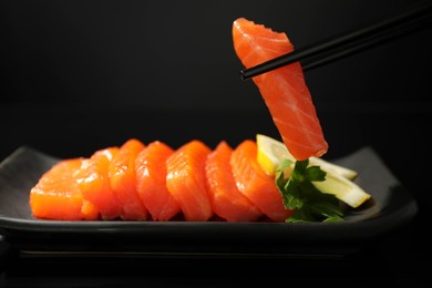 Photo of Taking delicious piece of salmon from serving board on black mirror surface, closeup. Tasty sashimi dish