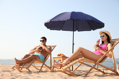 Couple with drinks resting on sunny beach at resort