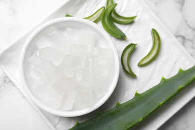 Photo of Aloe vera gel and slices of plant on white marble table, top view