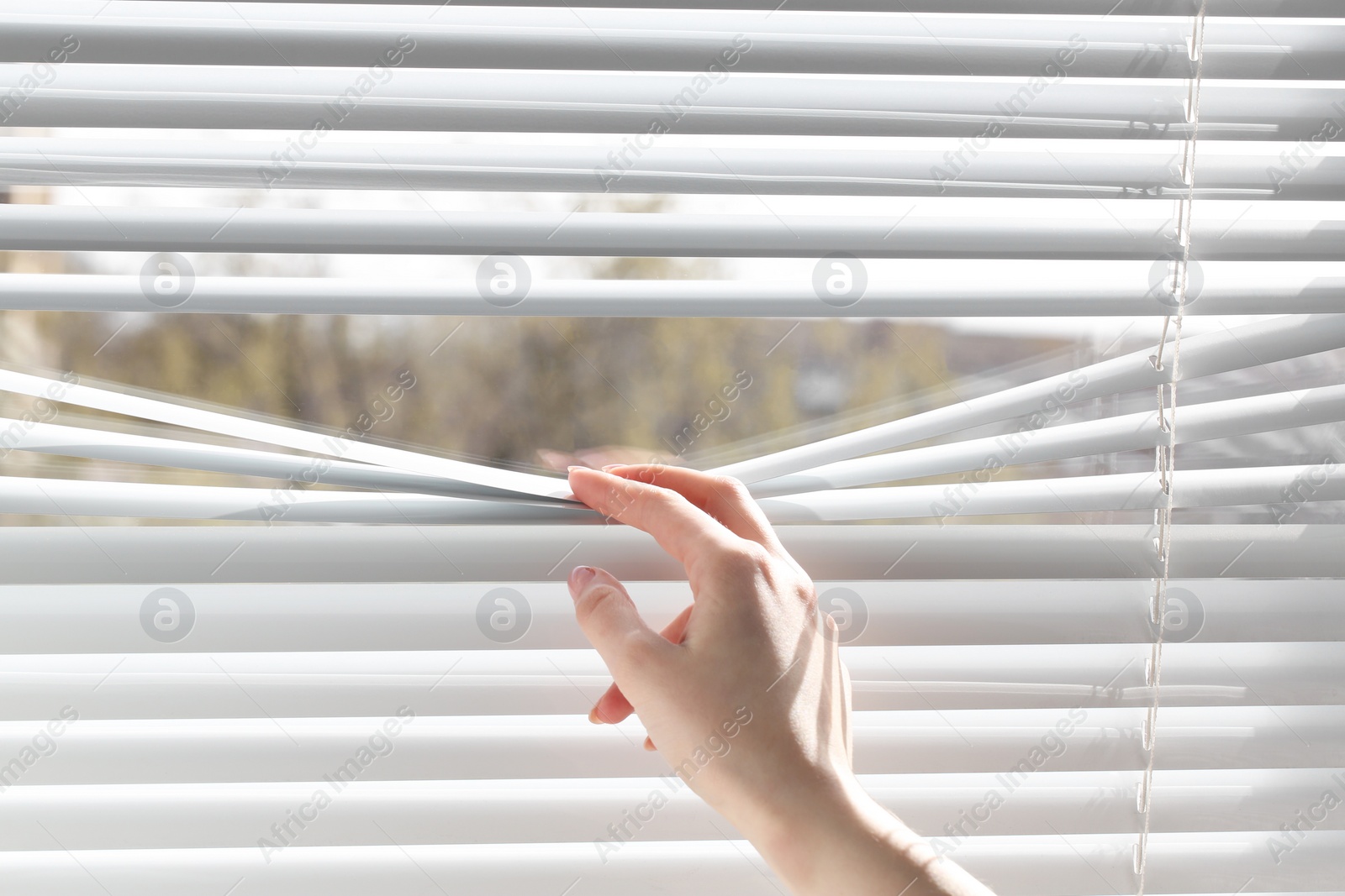 Photo of Woman separating slats of white blinds indoors, closeup