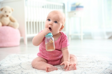 Photo of Pretty baby with bottle sitting on floor in room