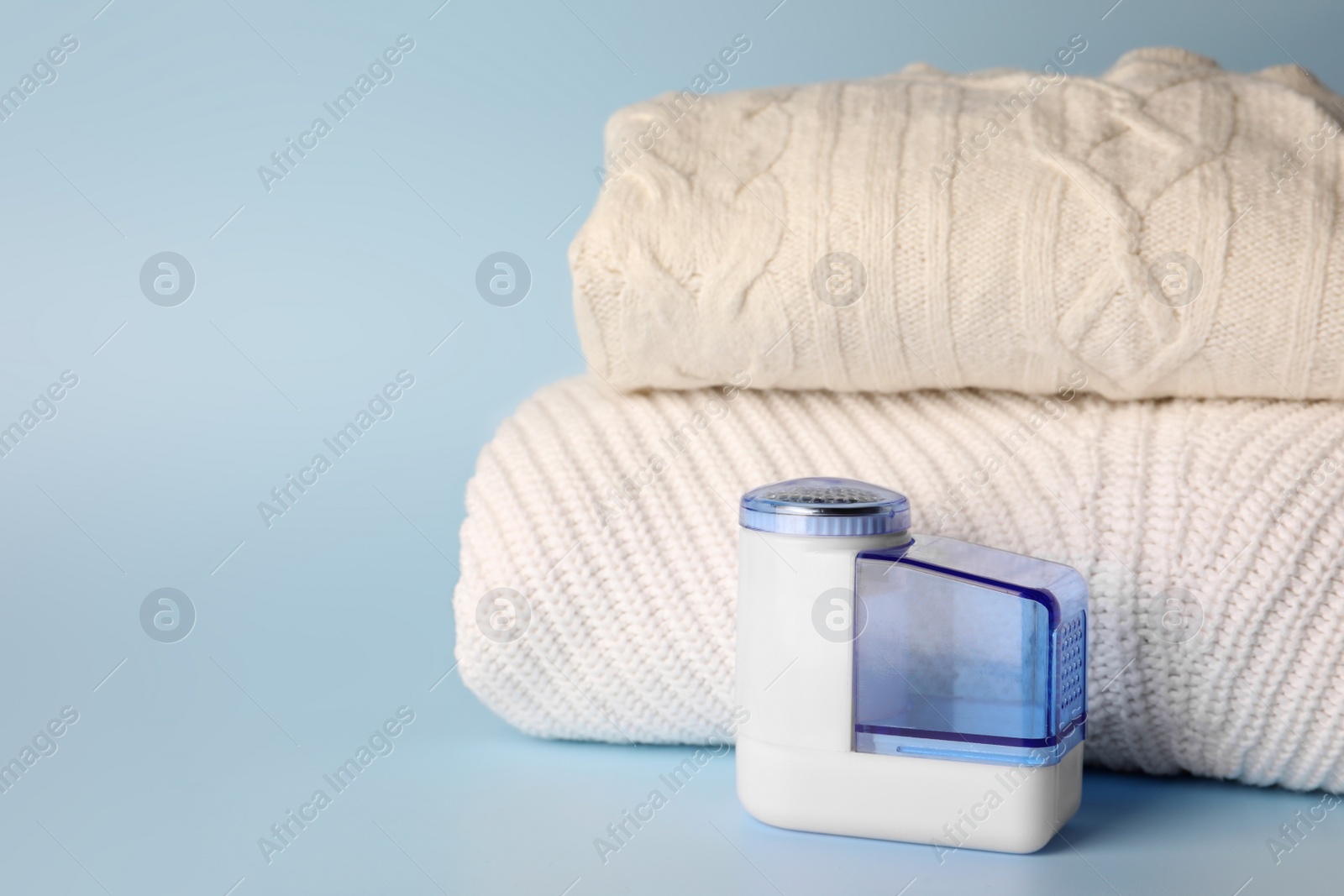 Photo of Modern fabric shaver and knitted clothes on light blue background, space for text